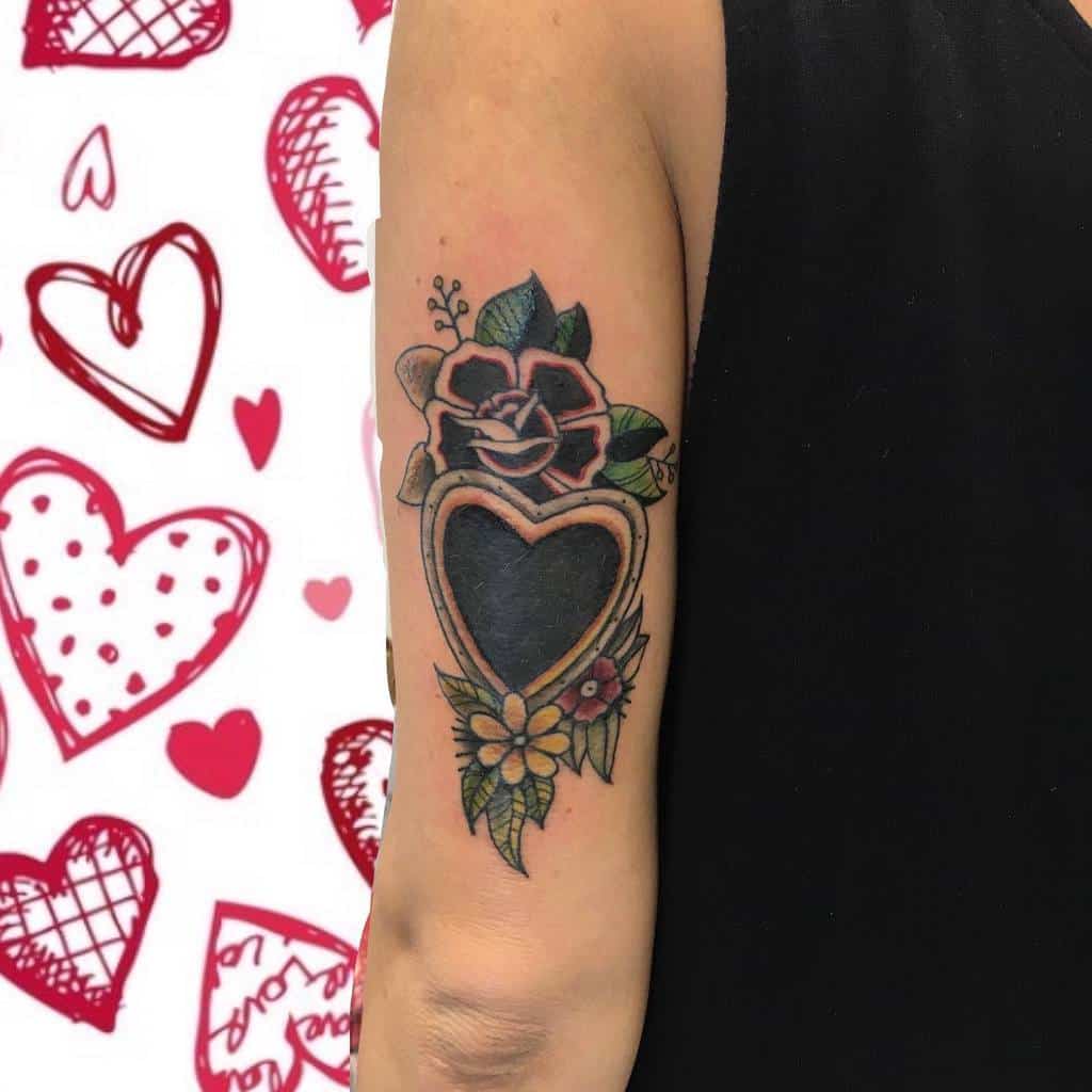 Traditional-style black heart tattoo with gold trim, floral accents, and a different flowers