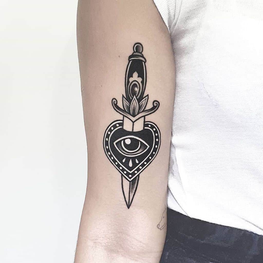 Bold black heart tattoo with an eye in the center, pierced by an ornate dagger