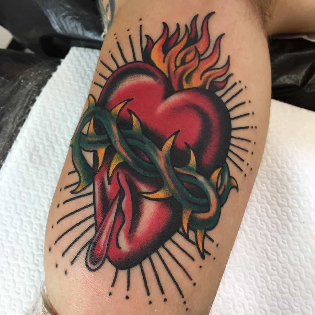 A tattoo of a bleeding, flaming heart wrapped in a thorny vine with rays emanating from it
