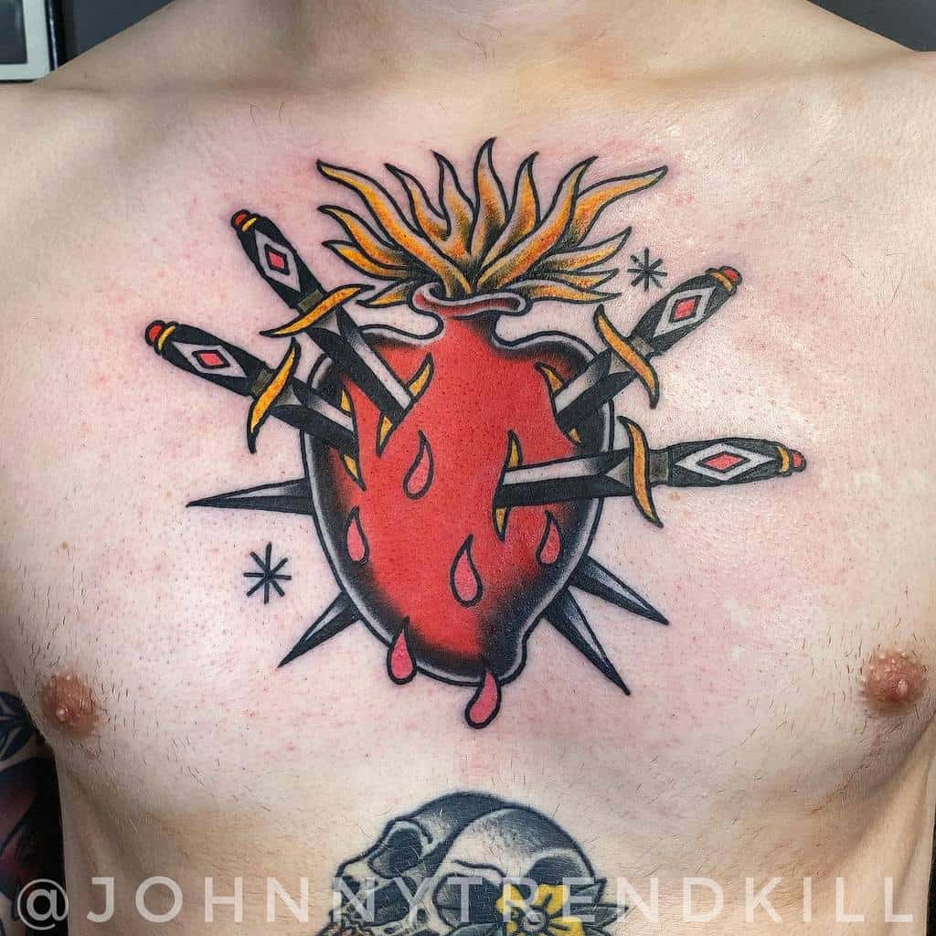 Tattoo of a red heart with flames on top and swords piercing it, bleeding slightly on a chest