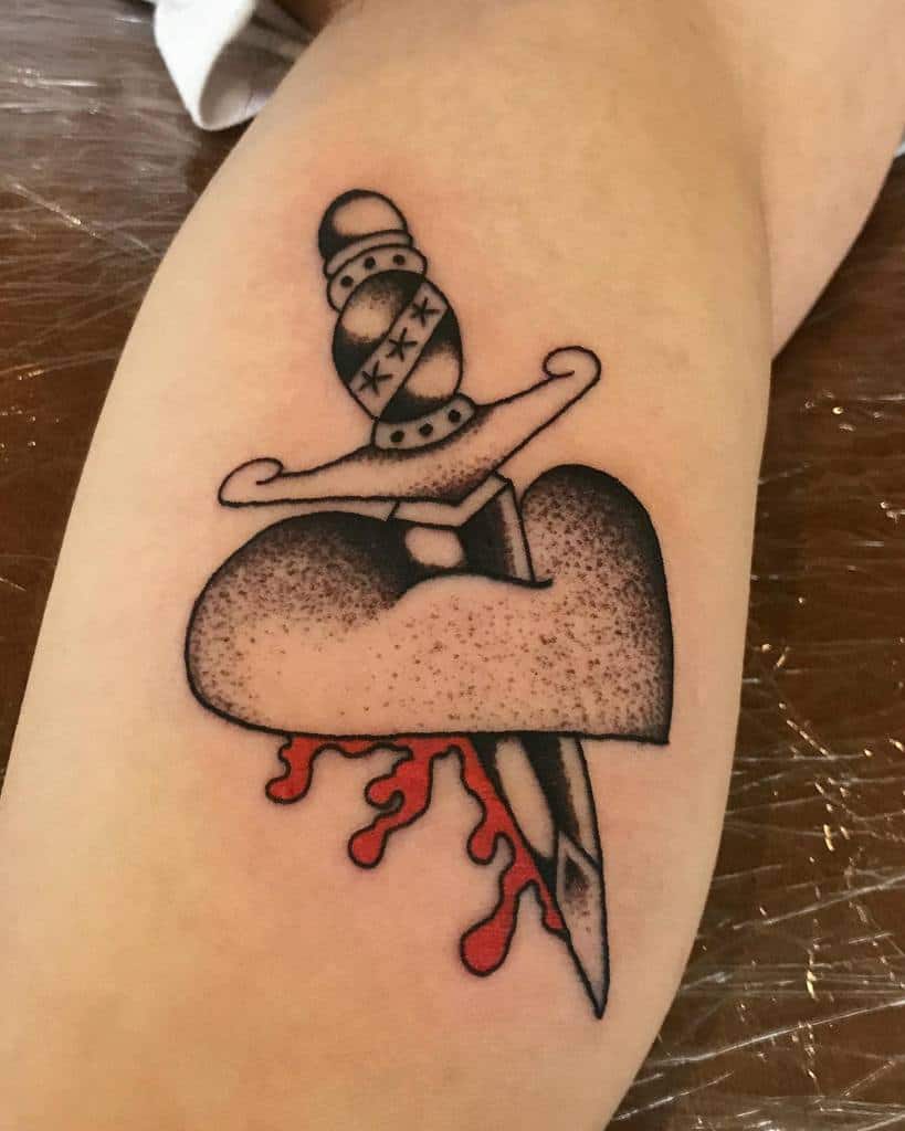 A tattoo of a dagger piercing a bleeding heart on an arm