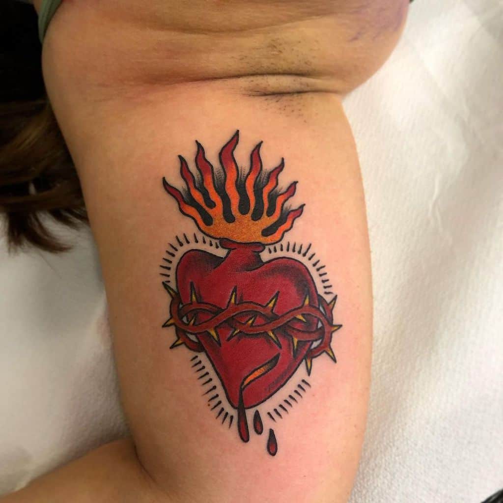A tattoo of a bleeding heart wrapped in flaming thorns with a drop of blood dripping from the bottom