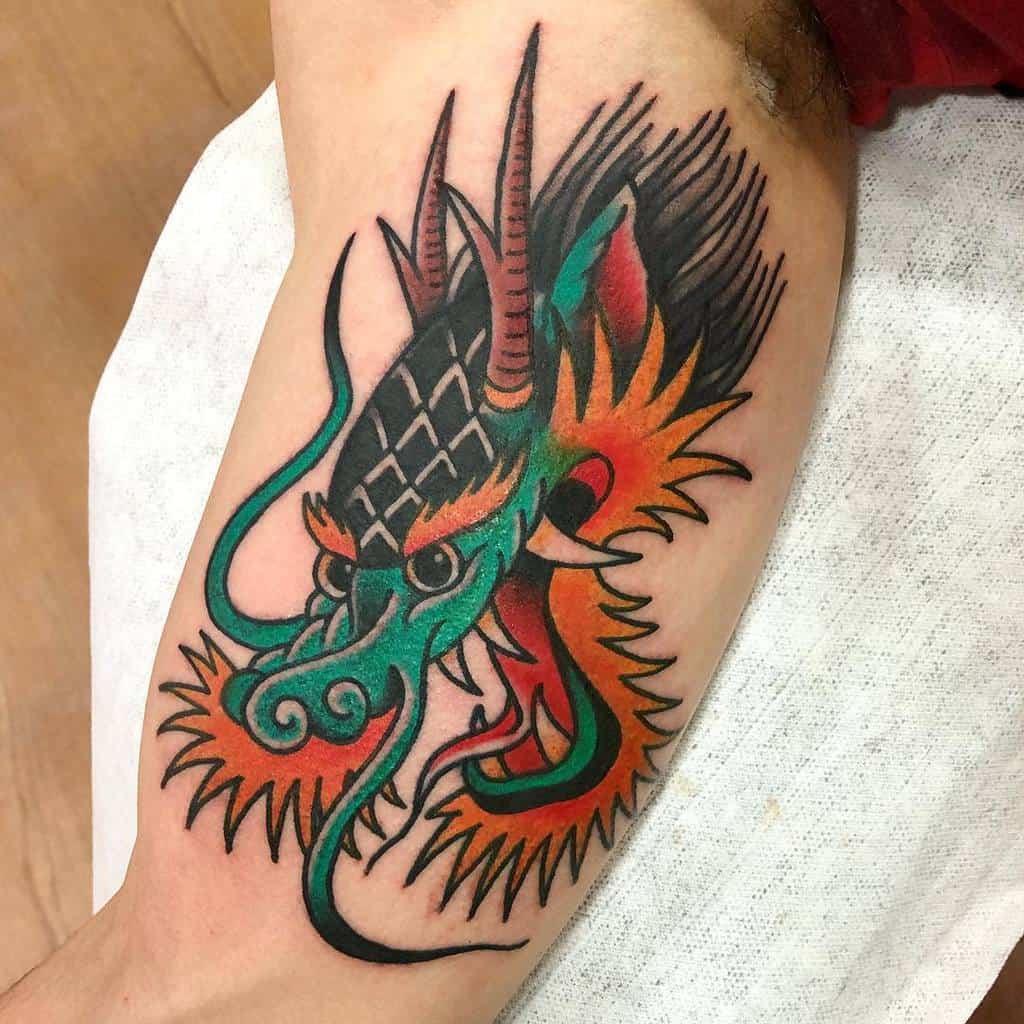 A traditional dragon tattoo featuring a striking head with green, red, and orange details adorns the person's arm