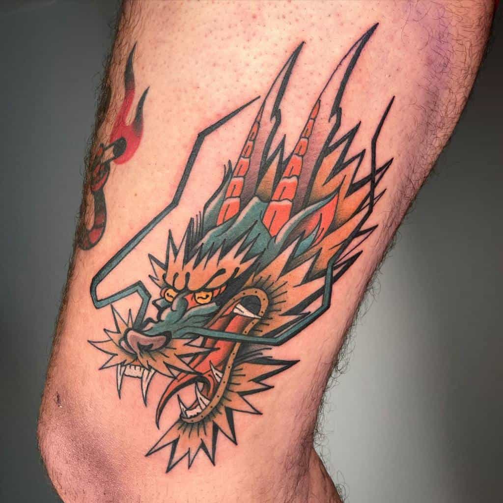 A colorful traditional dragon tattoo with a fierce head and sharp features, its open mouth displayed boldly on a person's leg