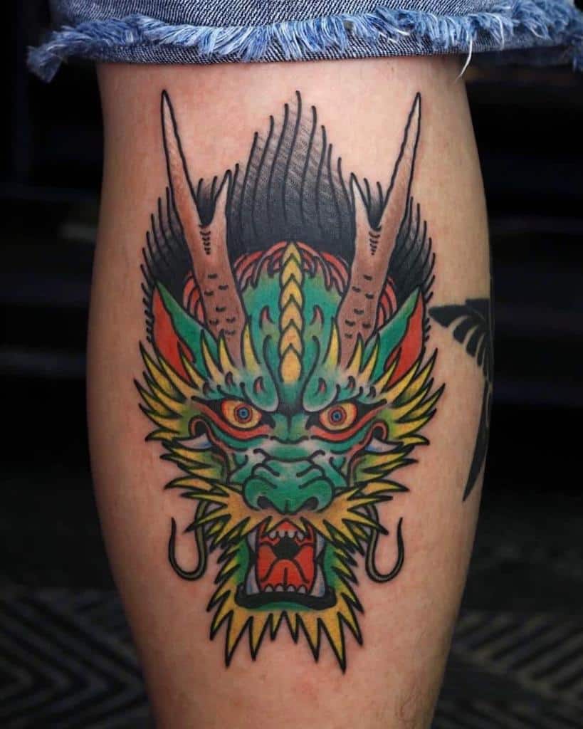 A traditional dragon head tattoo, with horns and an open mouth, adorns the leg