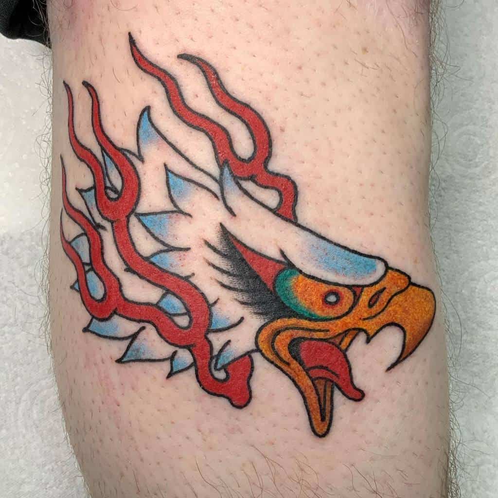 Tattoo of a stylized eagle head with red flames extending backward on a leg