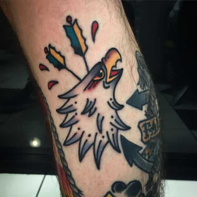 Tattoo of a stylized eagle head with arrows on an arm featuring bold lines and vibrant colors