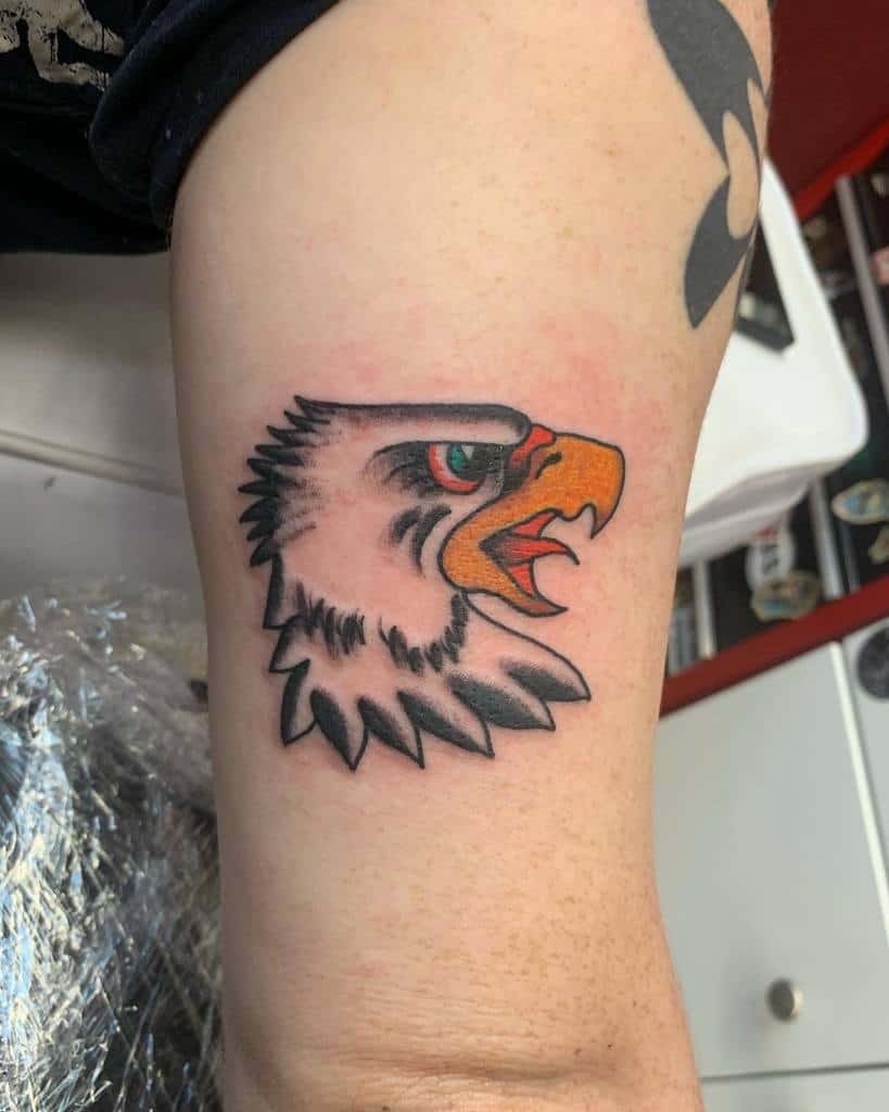 Tattoo of an eagle head on an upper arm, showing the bird with an open beak and vivid, bold colors