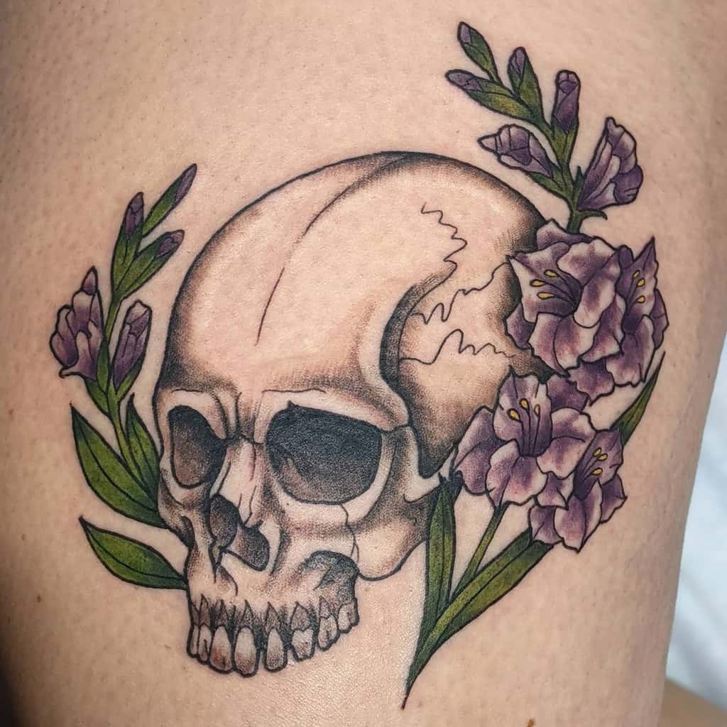 Tattoo of a skull adorned with purple gladiolus flowers and green leaves on the skin