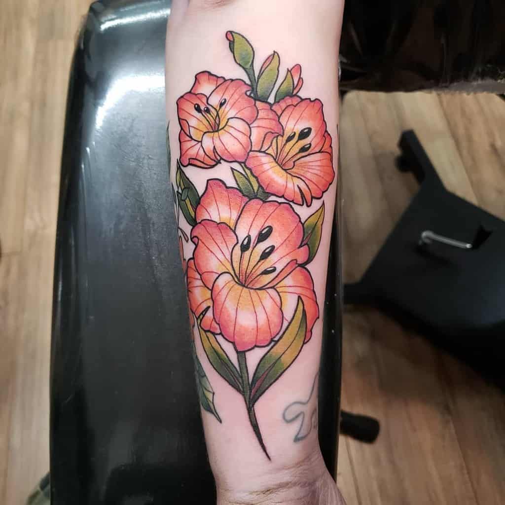 Forearm tattoo of vibrant red and orange gladiolus flowers with green leaves on light skin