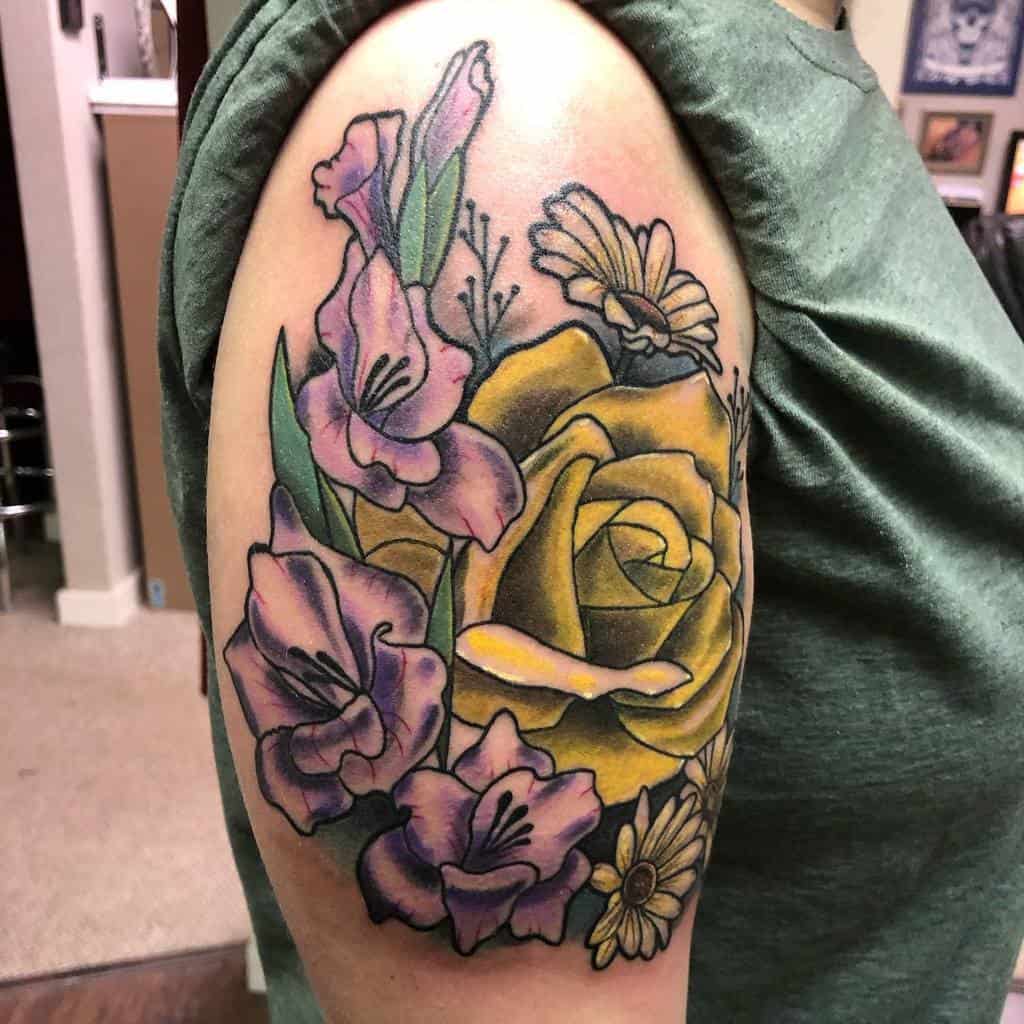 A colorful floral tattoo with roses, gladiolus, and other flowers adorns a person's upper arm