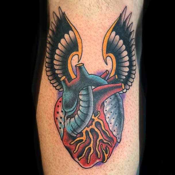 Tattoo of a detailed heart adorned with striking black and yellow wings on a person's skin