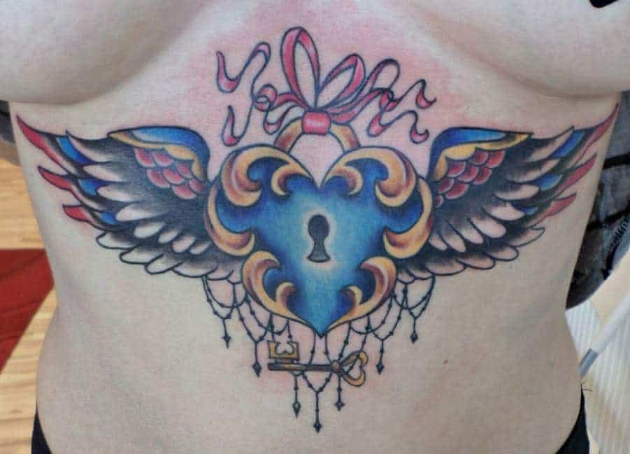 Tattoo of a vibrant, winged heart with a keyhole, ribbon, and key on a person's chest