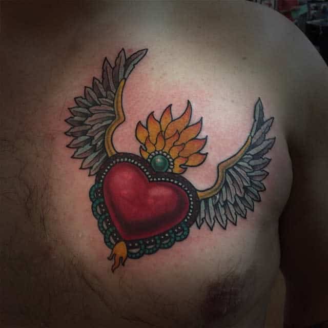 Tattoo of a heart with wings gently emerging from the flame on a person's chest