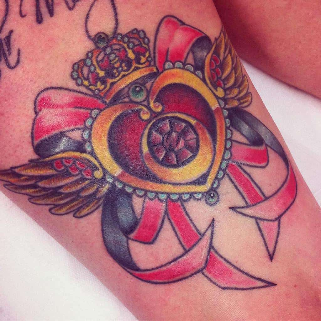 Colorful tattoo of a heart with wings, adorned with a crown and ribbon on skin