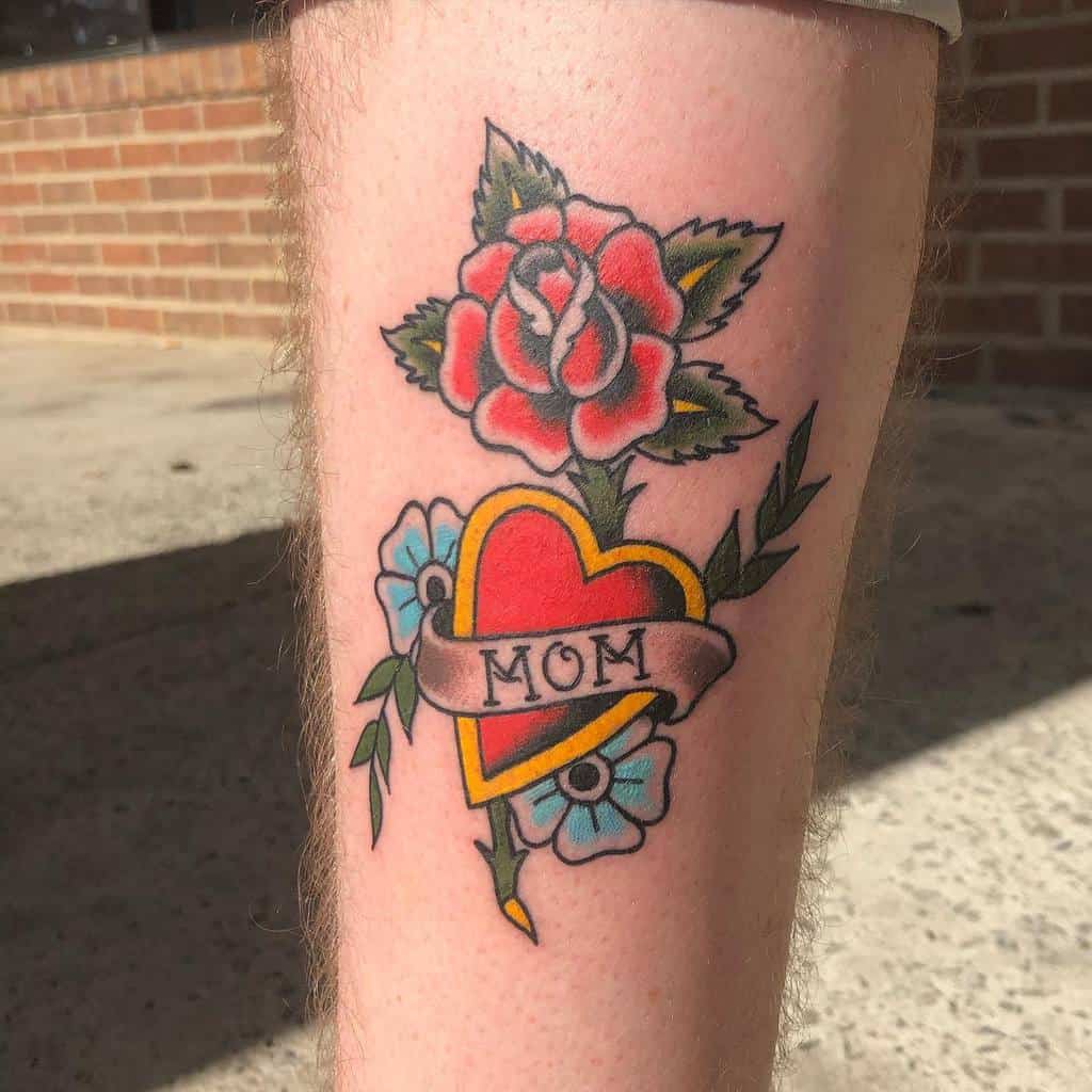 Tattoo of a heart adorned with the word "Mom," surrounded by delicate flowers and leaves, gracing an individual's arm