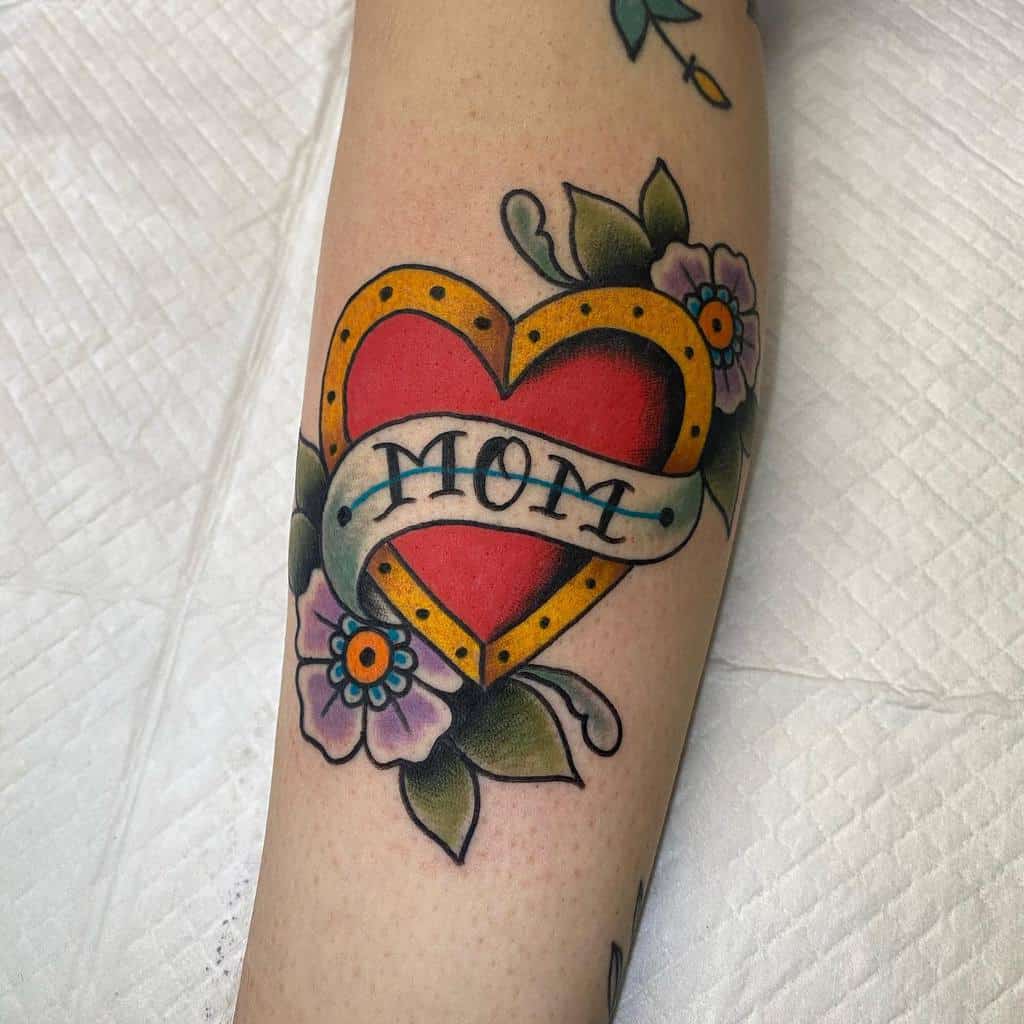 Tattoo of a heart with a banner reading "MOM" and flowers surrounding it on a forearm, capturing the essence of love and family