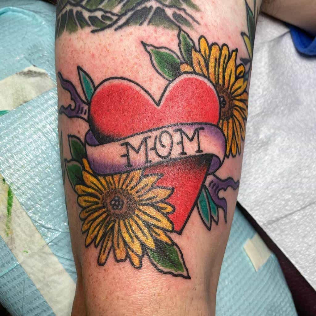 Tattoo of a vibrant red heart with a "Mom" banner, complemented by sunflowers and green leaves, gracefully depicted on an arm