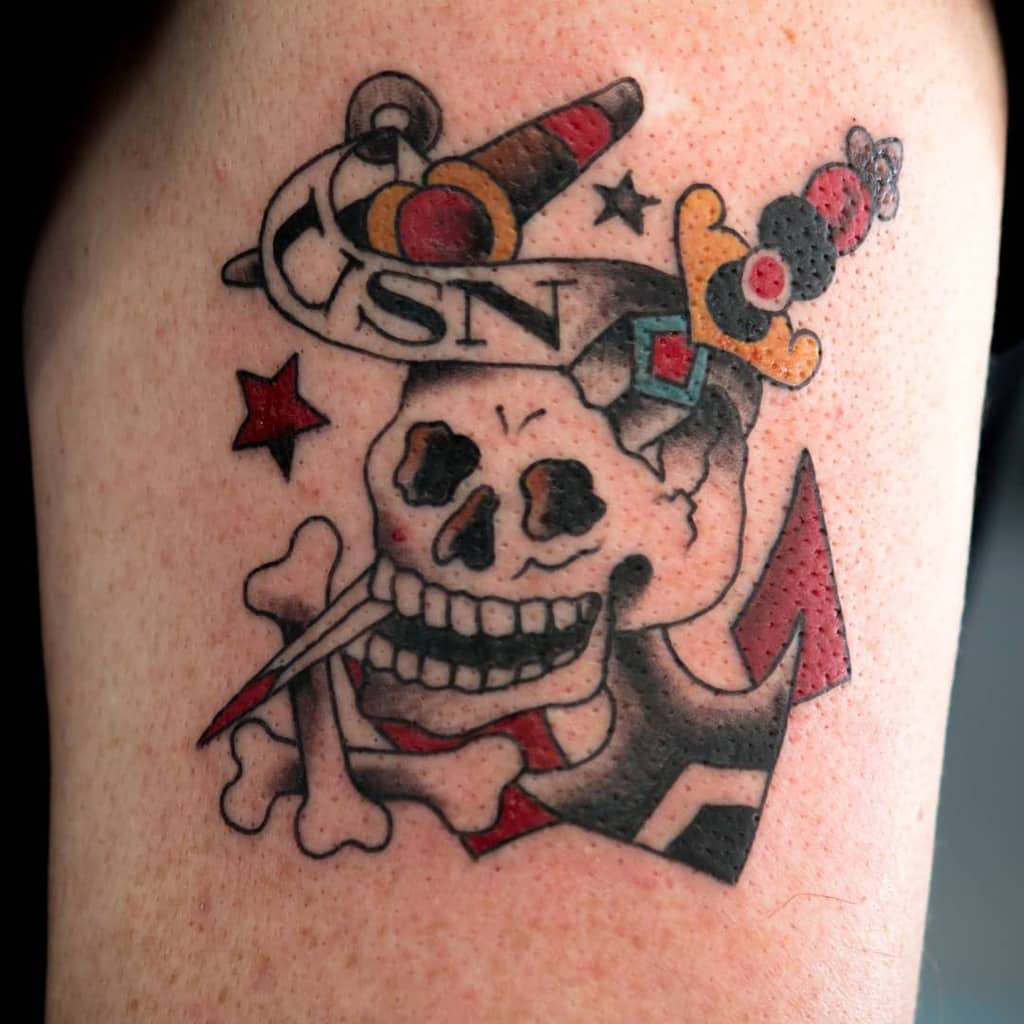 Tattoo of a skull and crossbones with a knife, wearing a hat with letters "USN" and an anchor, symbolizing the Navy