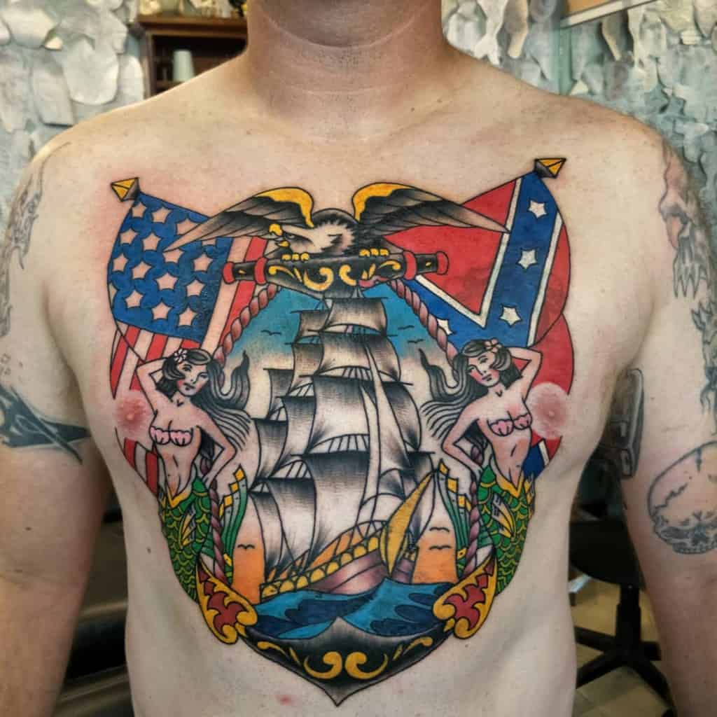 Colorful chest tattoo of a ship, mermaids, flags, an eagle, and a navy anchor