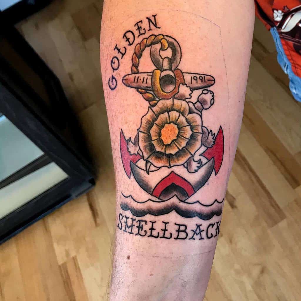 Tattoo of an anchor, turtle, and flower with text "GOLDEN SHELLBACK" on a person's arm, symbolizing a proud Navy tradition