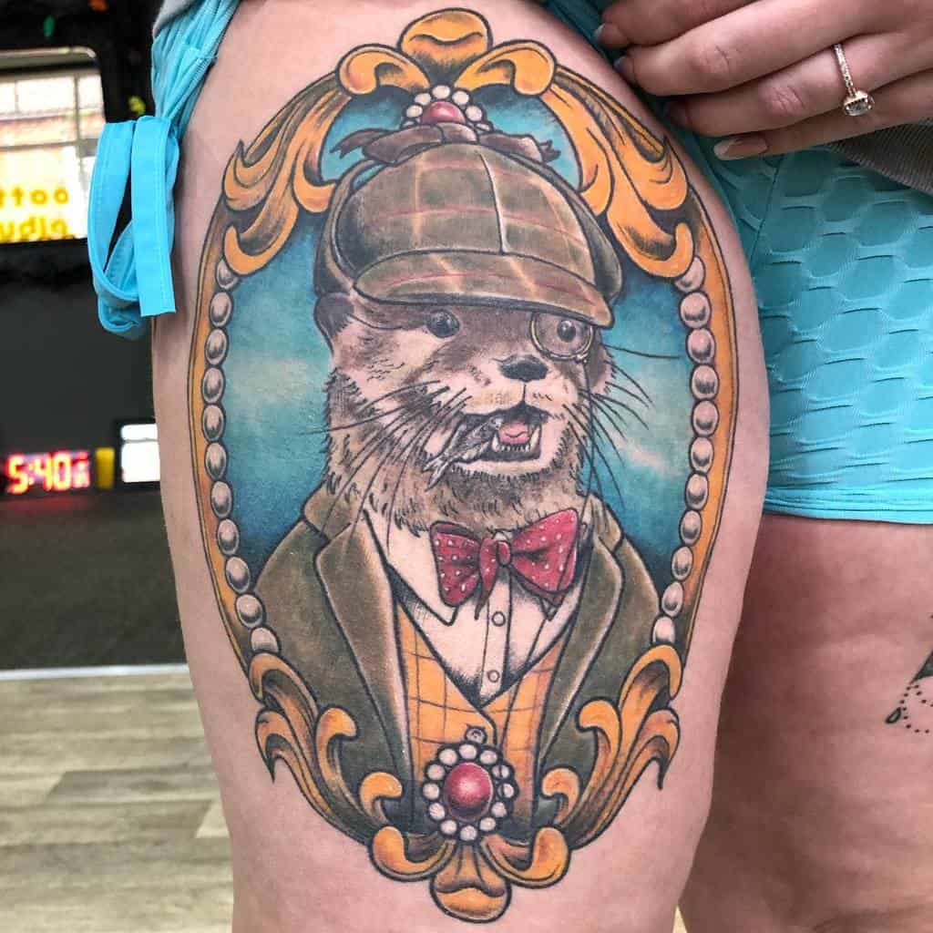 Tattoo of an otter dressed as a detective, wearing a hat and bow tie, with an ornate frame on a thigh