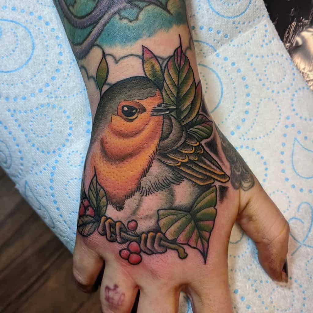 A colorful tattoo of a robin sitting on a branch with leaves and berries