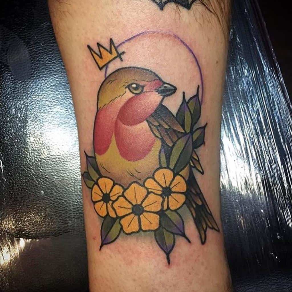 A colorful robin tattoo with a crown, surrounded by yellow flowers and green leaves, with violet circle line on the background