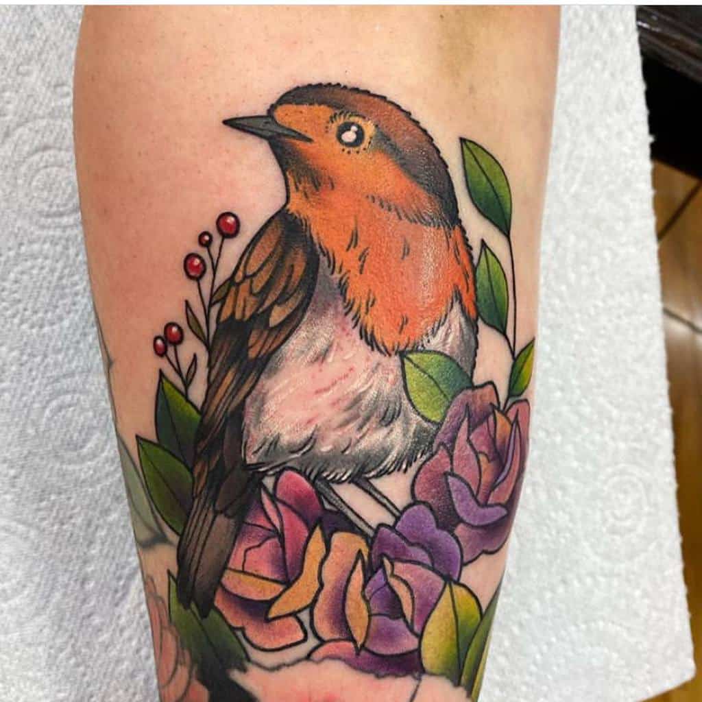 Colorful tattoo of a robin perched on a branch with red berries, surrounded by vibrant roses in shades of pink, purple, and yellow, with detailed shading on the robin