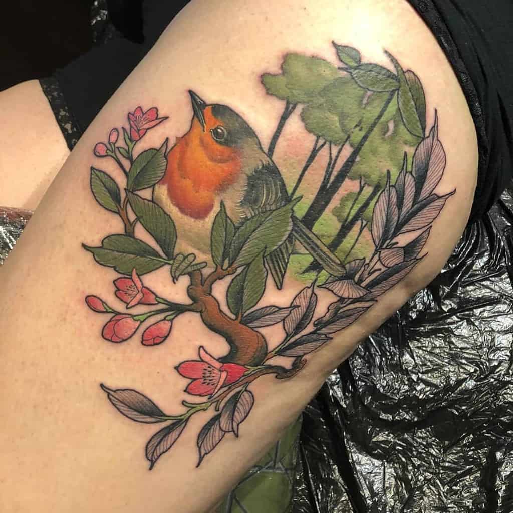 Colorful tattoo of a robin perched on a branch with pink flowers, surrounded by lush greenery and trees, with soft shading and naturalistic colors