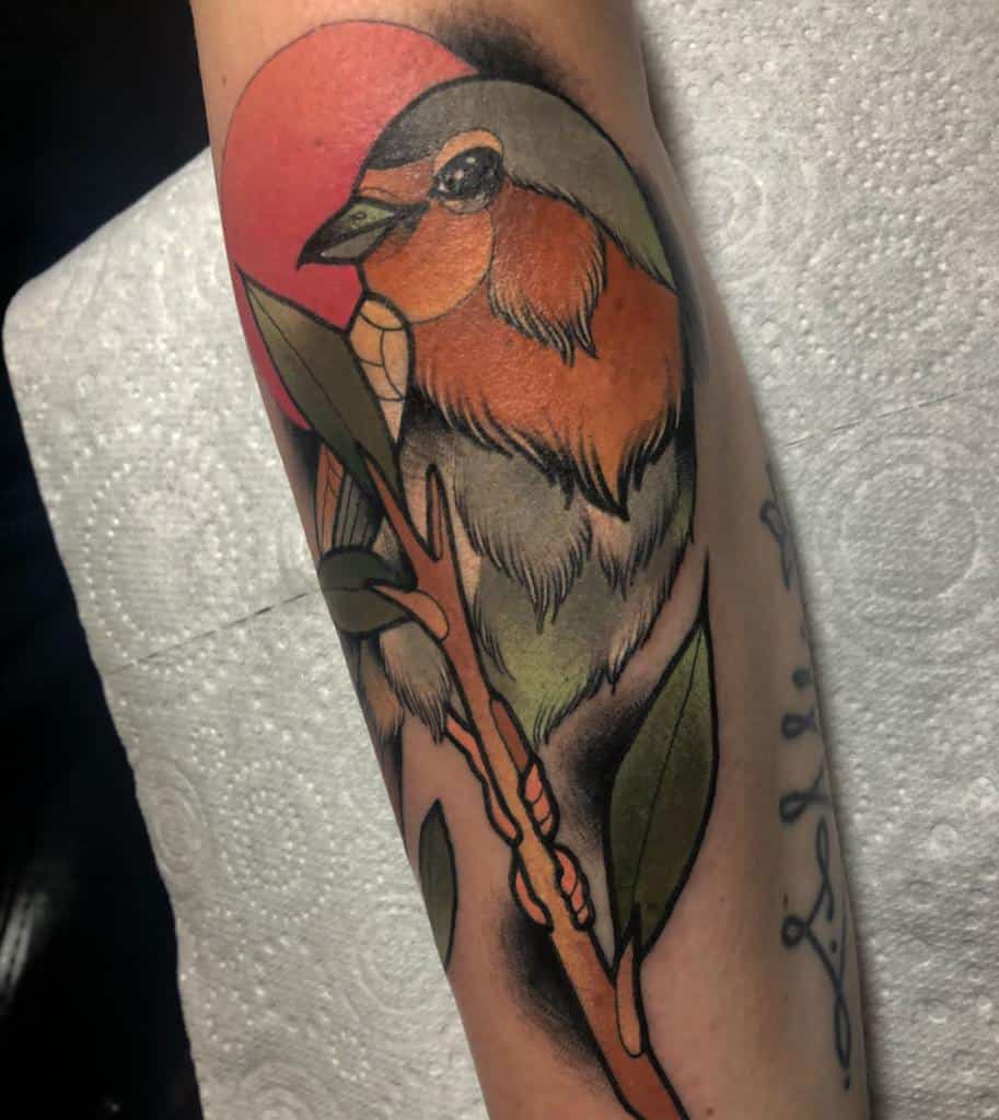 Tattoo of a colorful robin on a branch with green leaves, with a red sun in the background