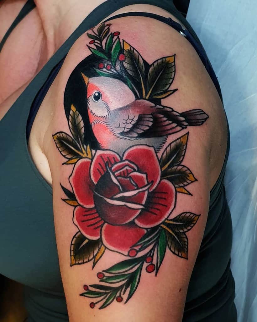 Tattoo of a robin perched on a rose with leaves, berries, and a black circle backdrop