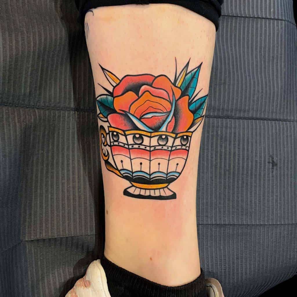 Colorful tattoo of a orange rose in a decorative teacup, depicted with bold outlines and vivid colors