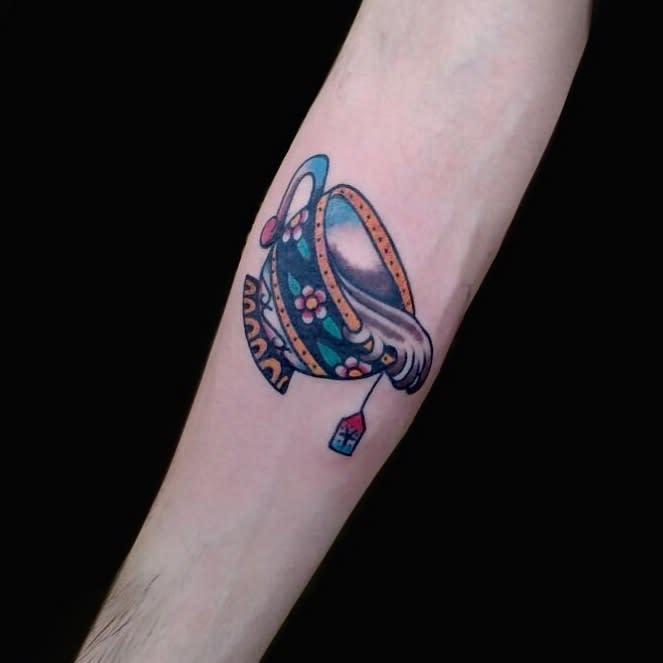Tattoo of a colorful floral teacup, pouring liquid with a tea bag attached