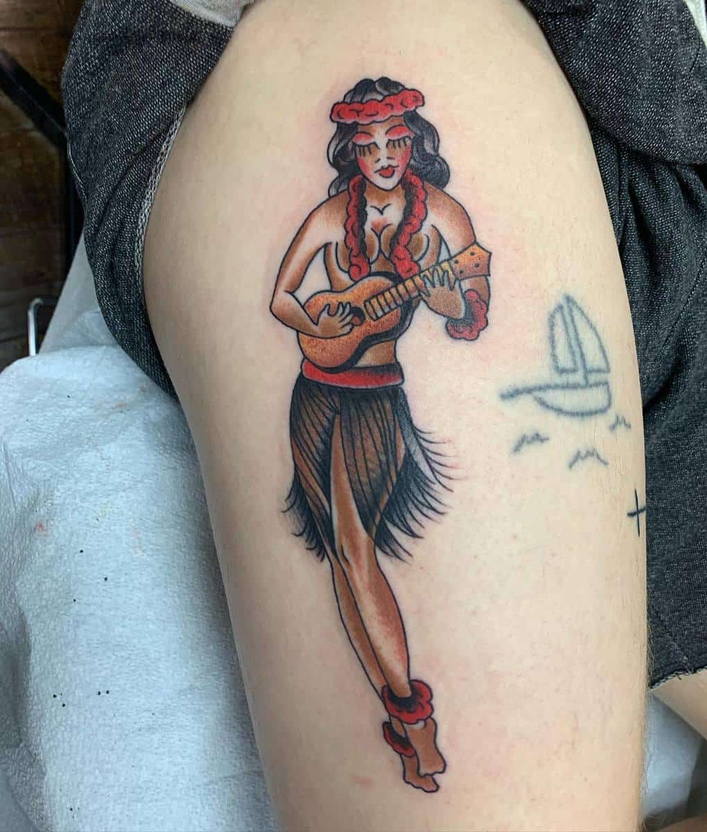 Tattoo of a hula dancer wearing a grass skirt and lei, playing a ukulele on an upper thigh