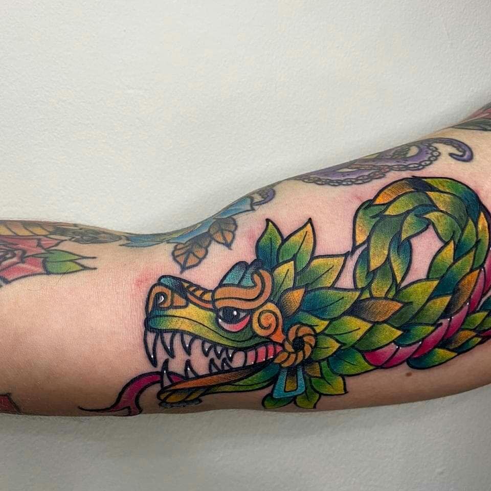 Colorful bicep tattoo of Quetzalcoatl with vibrant feathers and bold outlines