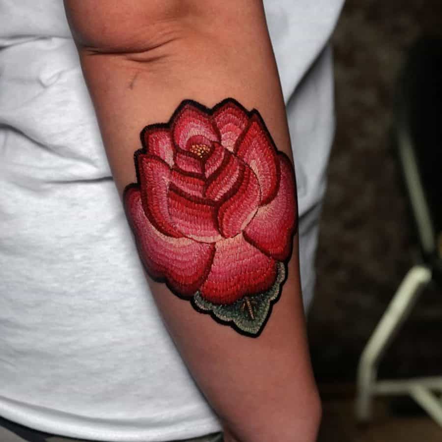 Textile-effect tattoo of a red rose, blending intricate threadwork with a fabric-inspired aesthetic for a unique patchwork feel.