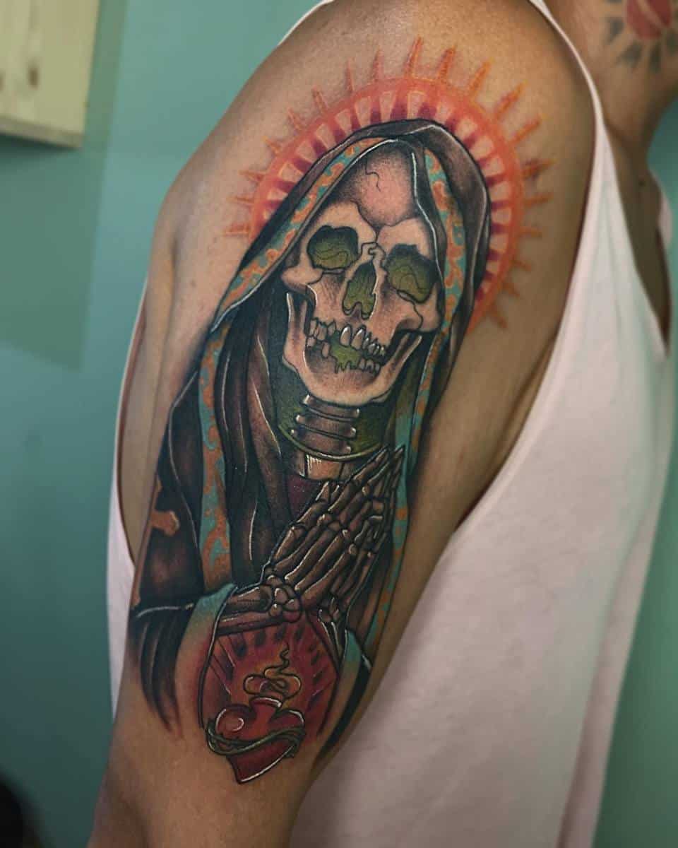 Colorful Santa Muerte tattoo on the upper arm featuring a radiant orange halo and detailed sacred heart