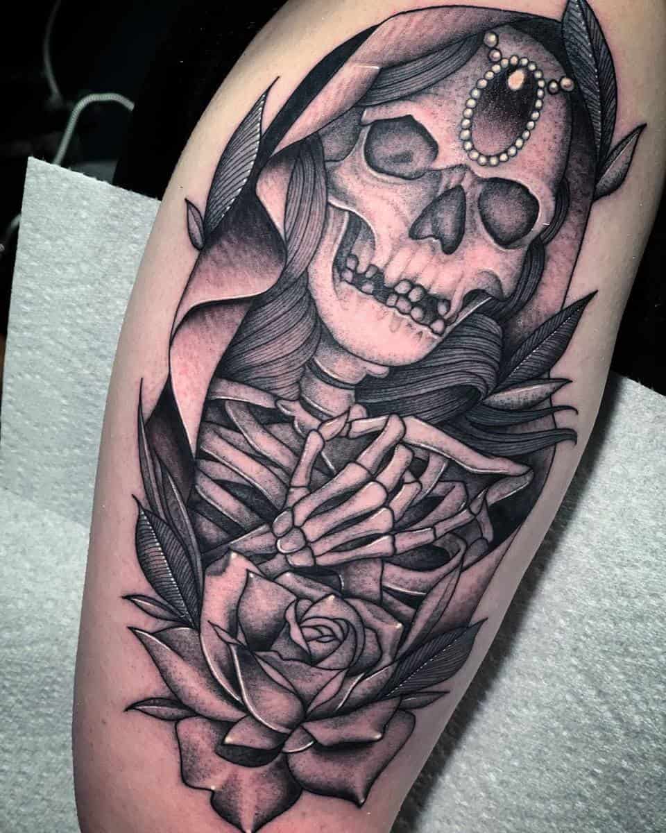 This black and grey Santa Muerte tattoo showcases intricate linework, featuring a skeletal figure with delicate shading and a rose, symbolizing life and death intertwined in a bold yet elegant design