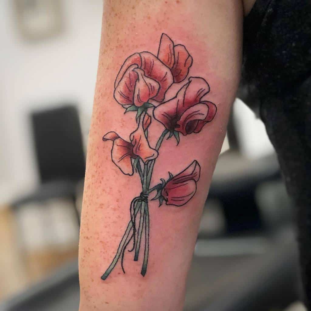 Traditional-style sweet pea flower tattoo with vibrant pink petals and detailed green stems on the arm