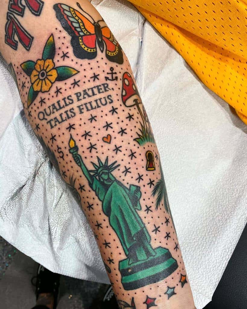 Traditional tattoo design featuring the Statue of Liberty, a butterfly, a flower, a mushroom, and the Latin phrase 'Qualis pater, talis filius' surrounded by stars.