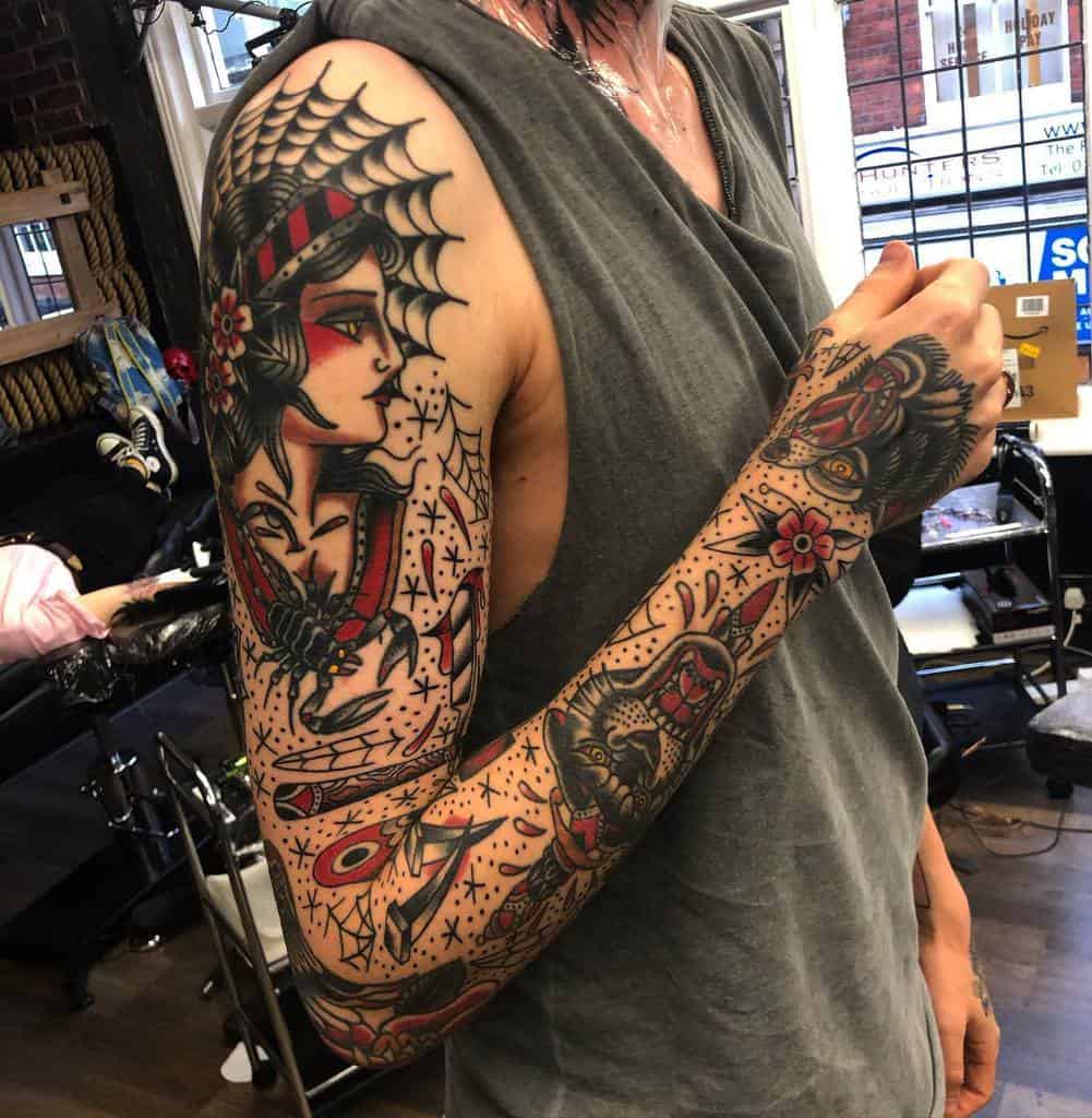 Traditional tattoo sleeve featuring a bold female portrait with a spider web, intricate hand and floral designs, and a wolf on the forearm