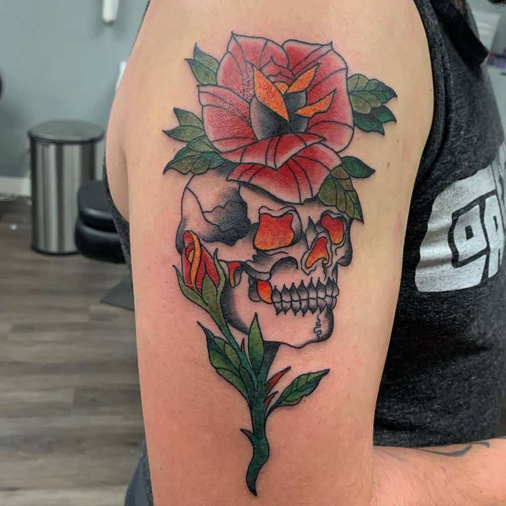 Tattoo of a skull with a red rose and green leaves on an upper arm