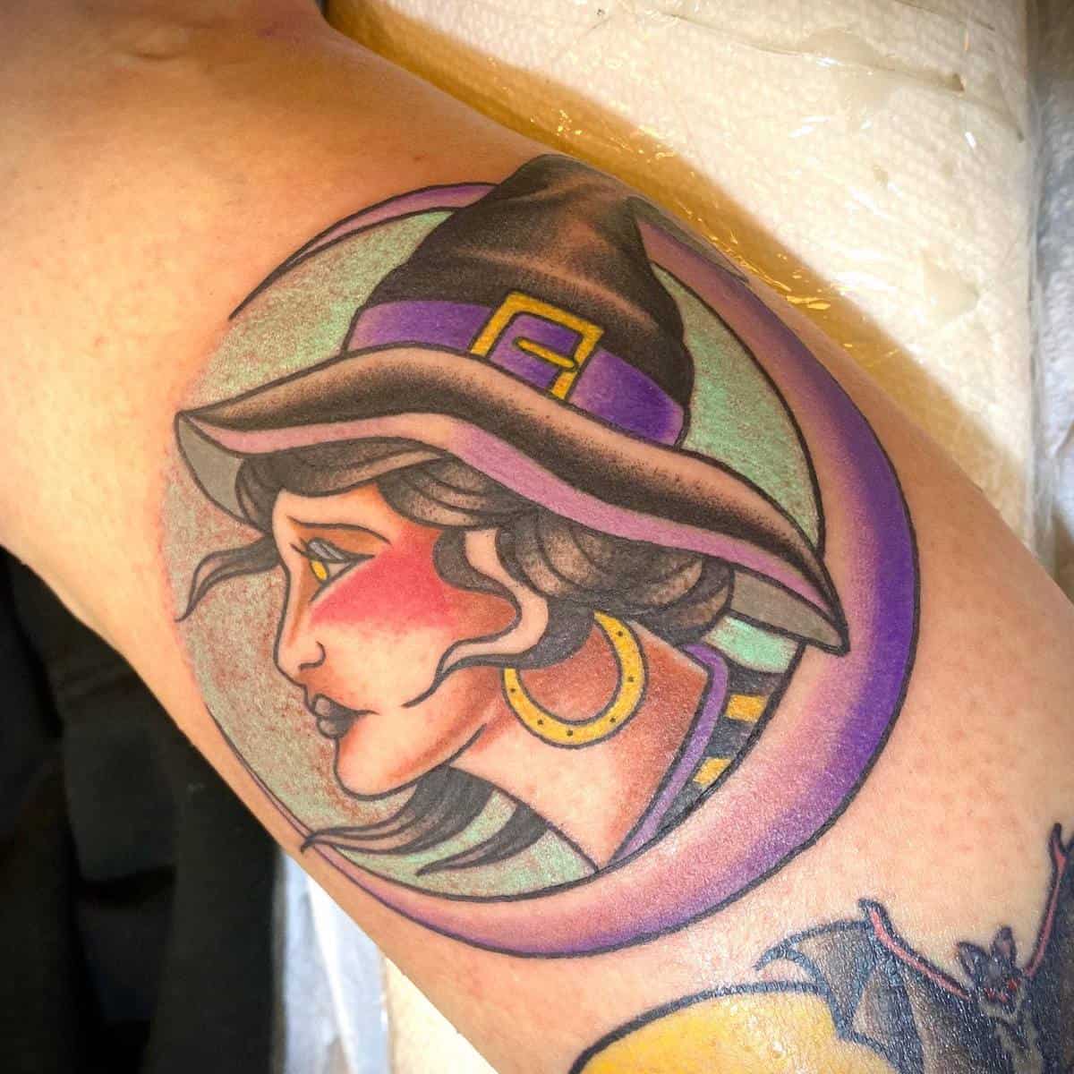 Tattoo of a witch in a hat with a crescent moon background on an arm