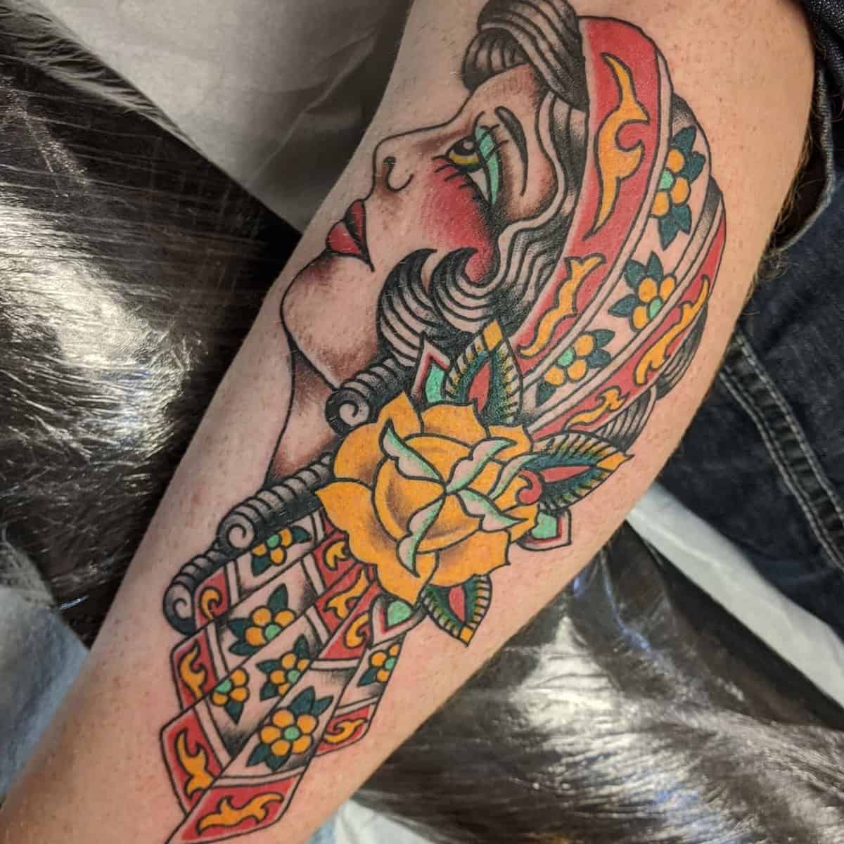 Colorful tattoo of a woman's face in profile, with a headscarf and a yellow rose on a forearm