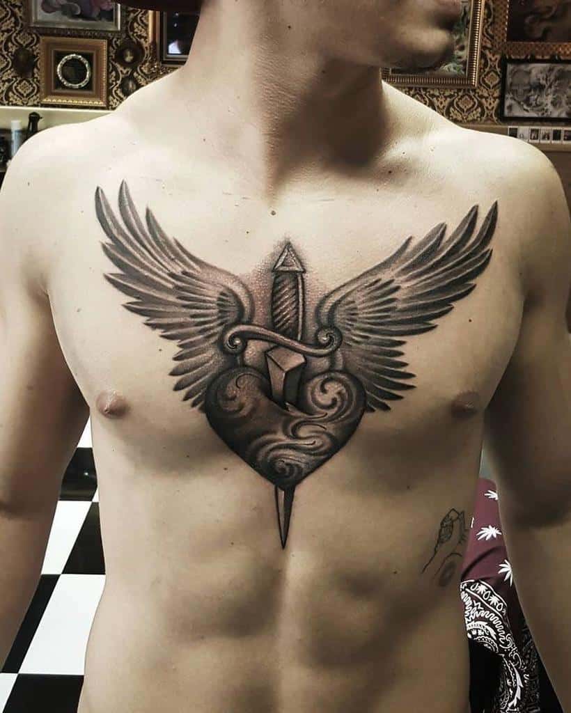 Black and gray tattoo of a heart with detailed wings and a dagger piercing through it