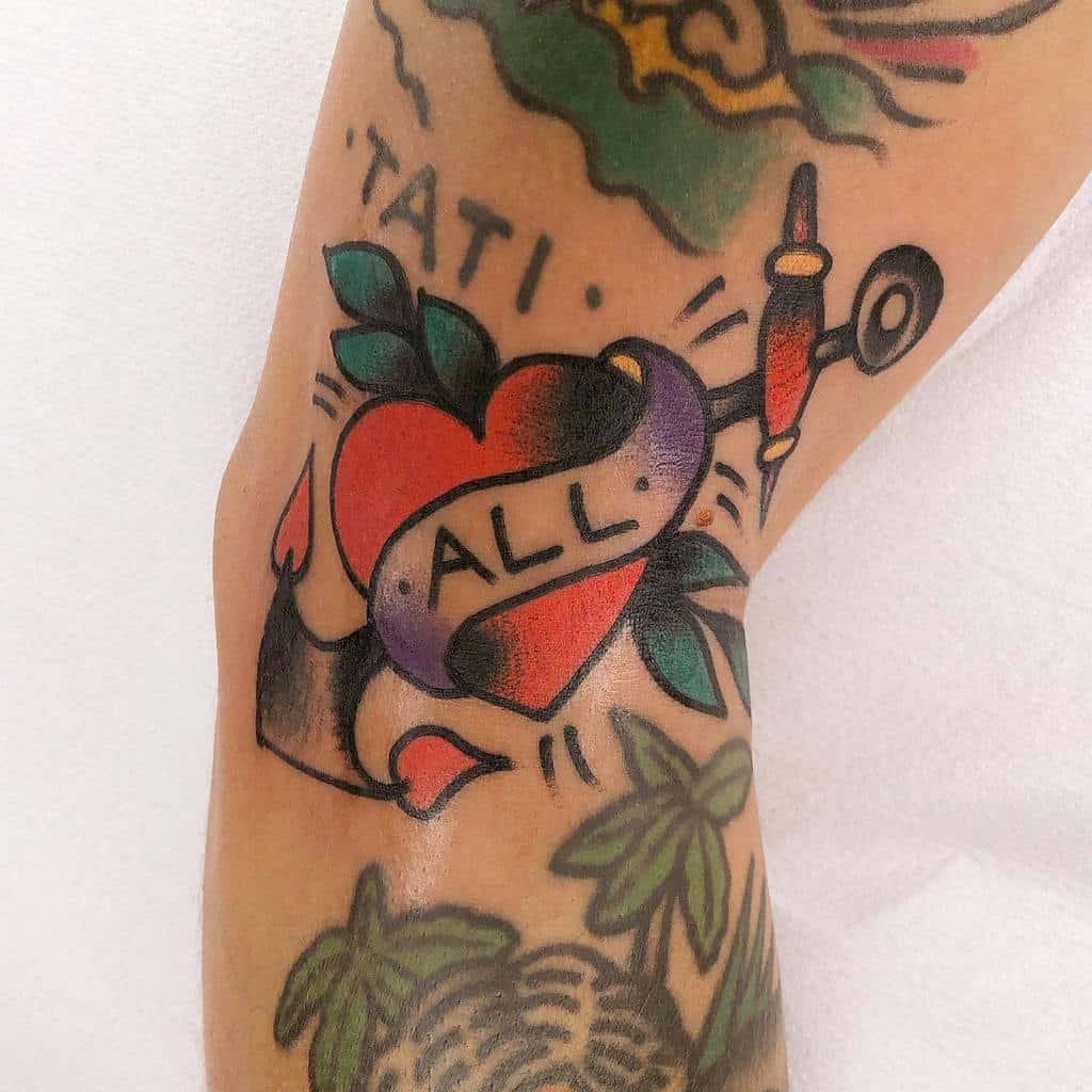 Traditional tattoo of a red heart with a banner reading 'ALL,' a tattoo machine, green leaves, and bold black shading