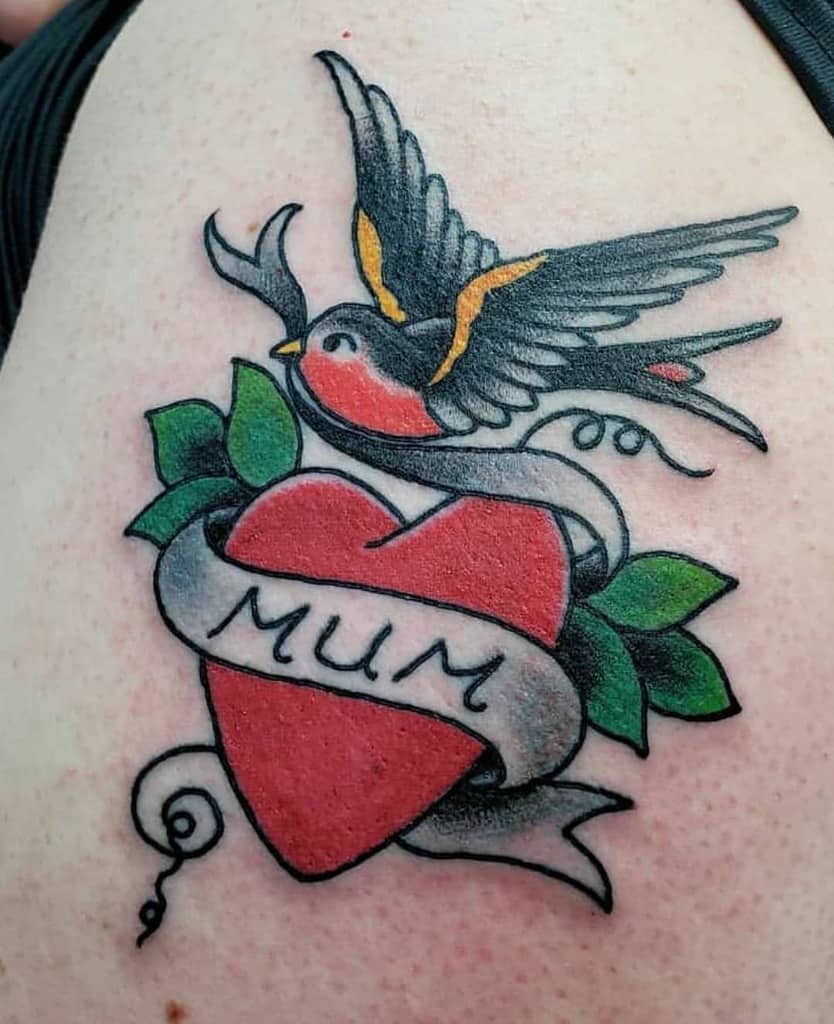 Tattoo of a swallow above a red heart with green leaves, wrapped in a banner that reads "MUM