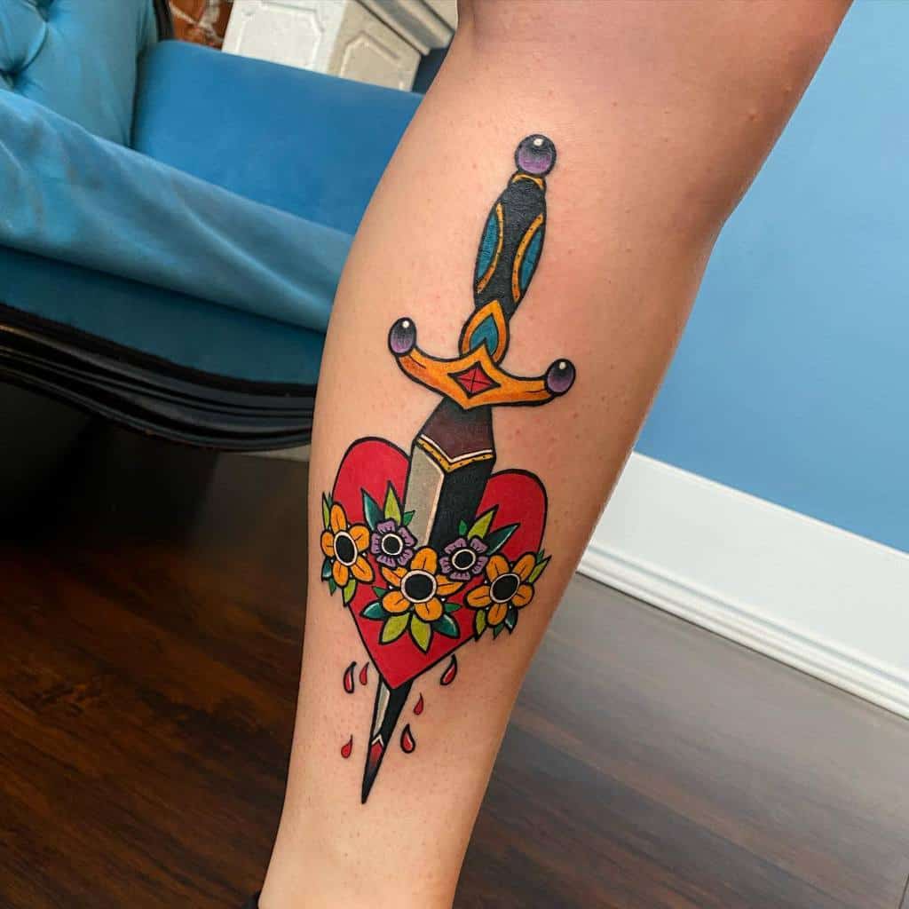 A colorful tattoo of a dagger piercing a red heart, adorned with flowers and dripping blood