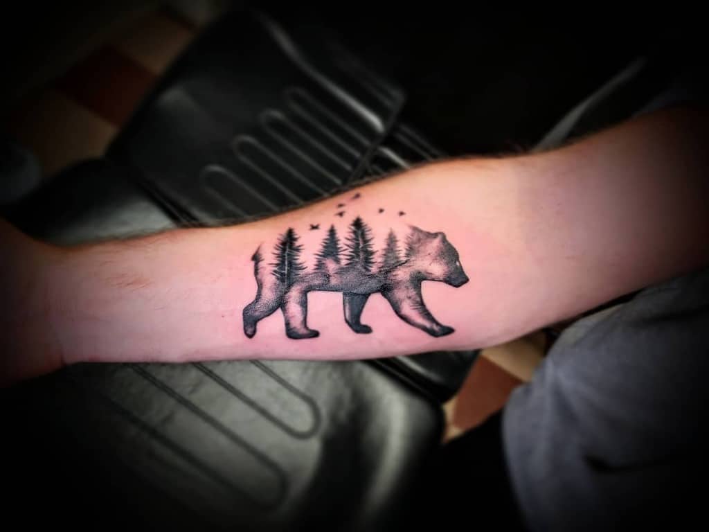 Tattoo of a bear filled with trees and stars, located on a forearm